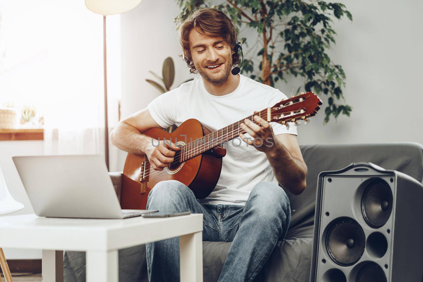 Young man watching guitar tutorial on his laptop at home