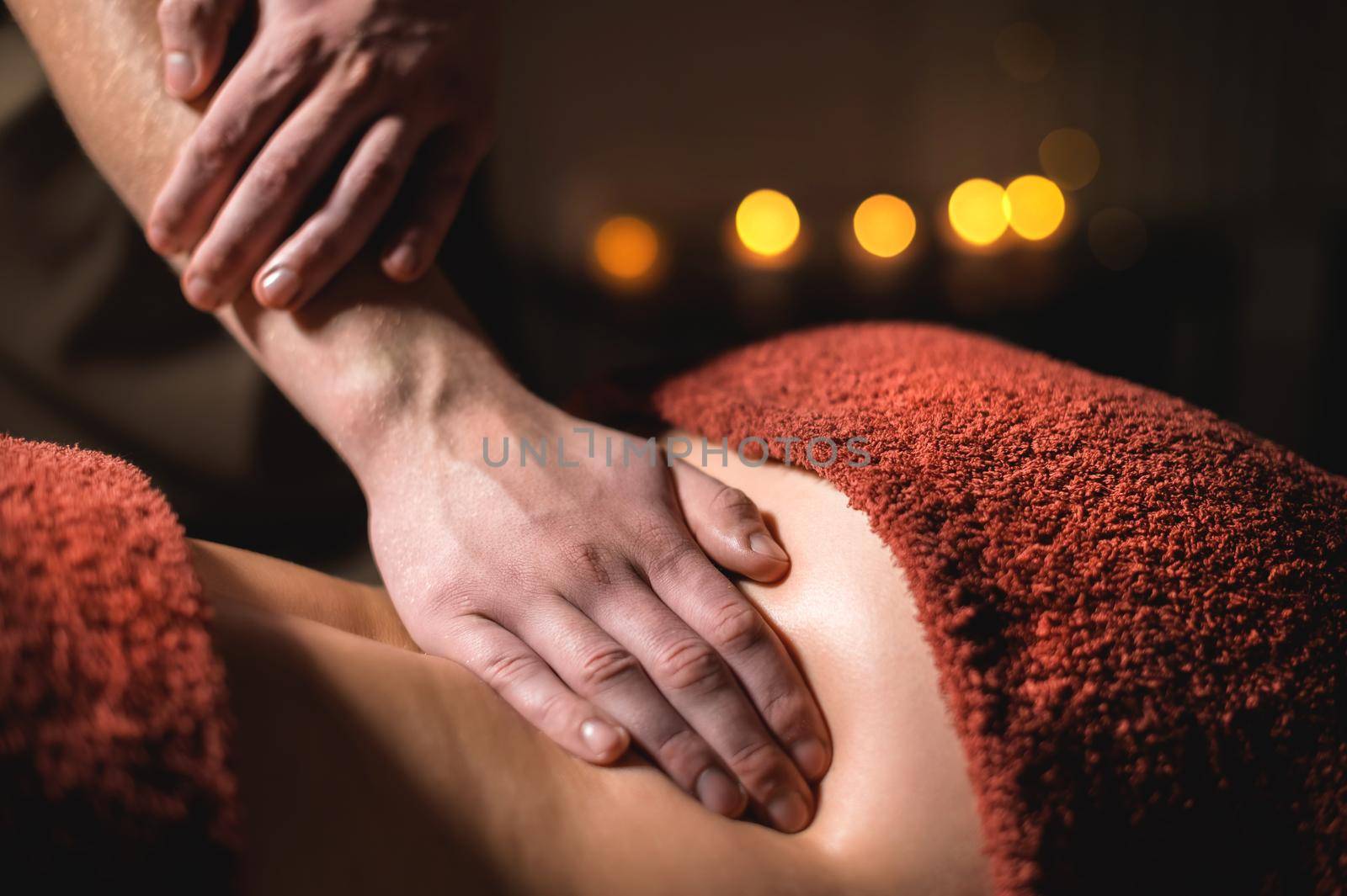 Professional premium massage in a dark atmospheric cabinet. Close-up hands Young man doing massage to a female client in a dark office on the background of burning candles.