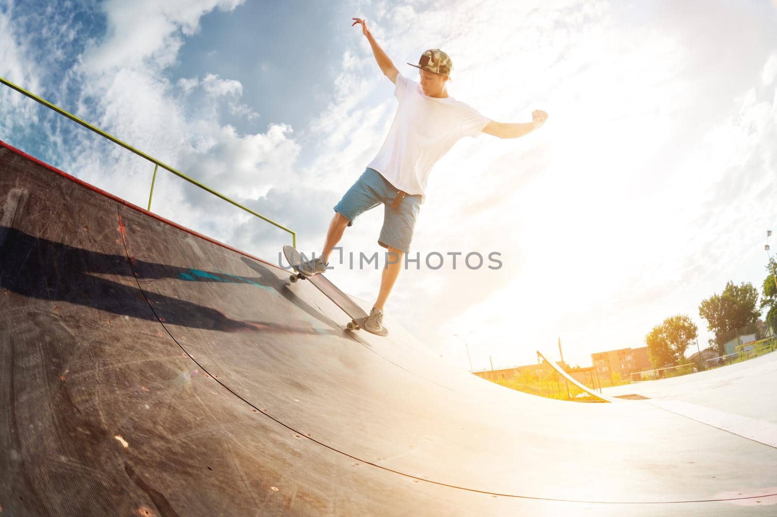 Portrait of a young skateboarder doing a trick on his skateboard on a halfpipe ramp in a skate park in the summer on a sunny day. The concept of youth culture of leisure and sports.