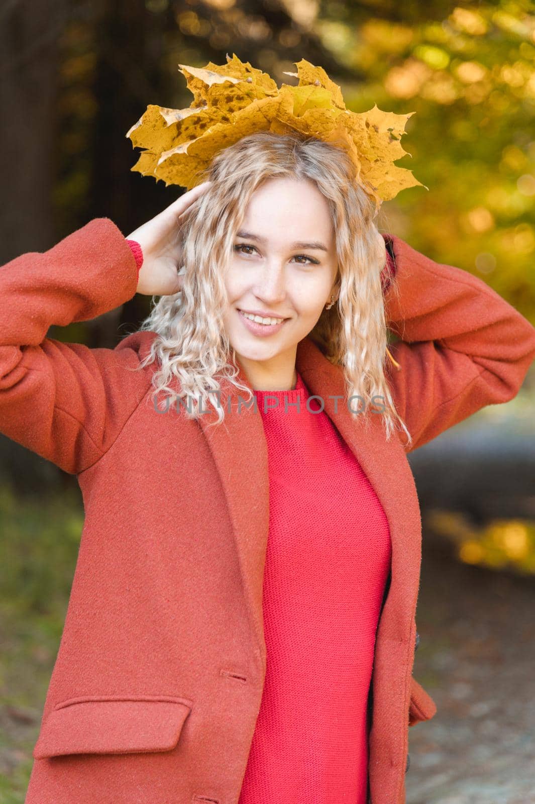 Portrait of attractive caucasian young blonde girl in red coat with a bouquet of fallen yellow leaves smiling in the autumn forest. The concept of autumn and fall holidays and weekends.