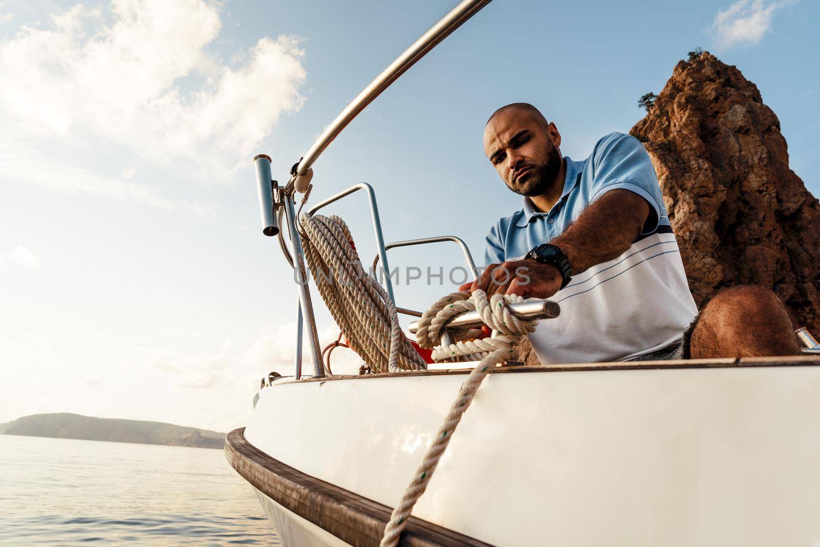 Young african american sailor tying ropes on sailboat in the sea on sunset, close up