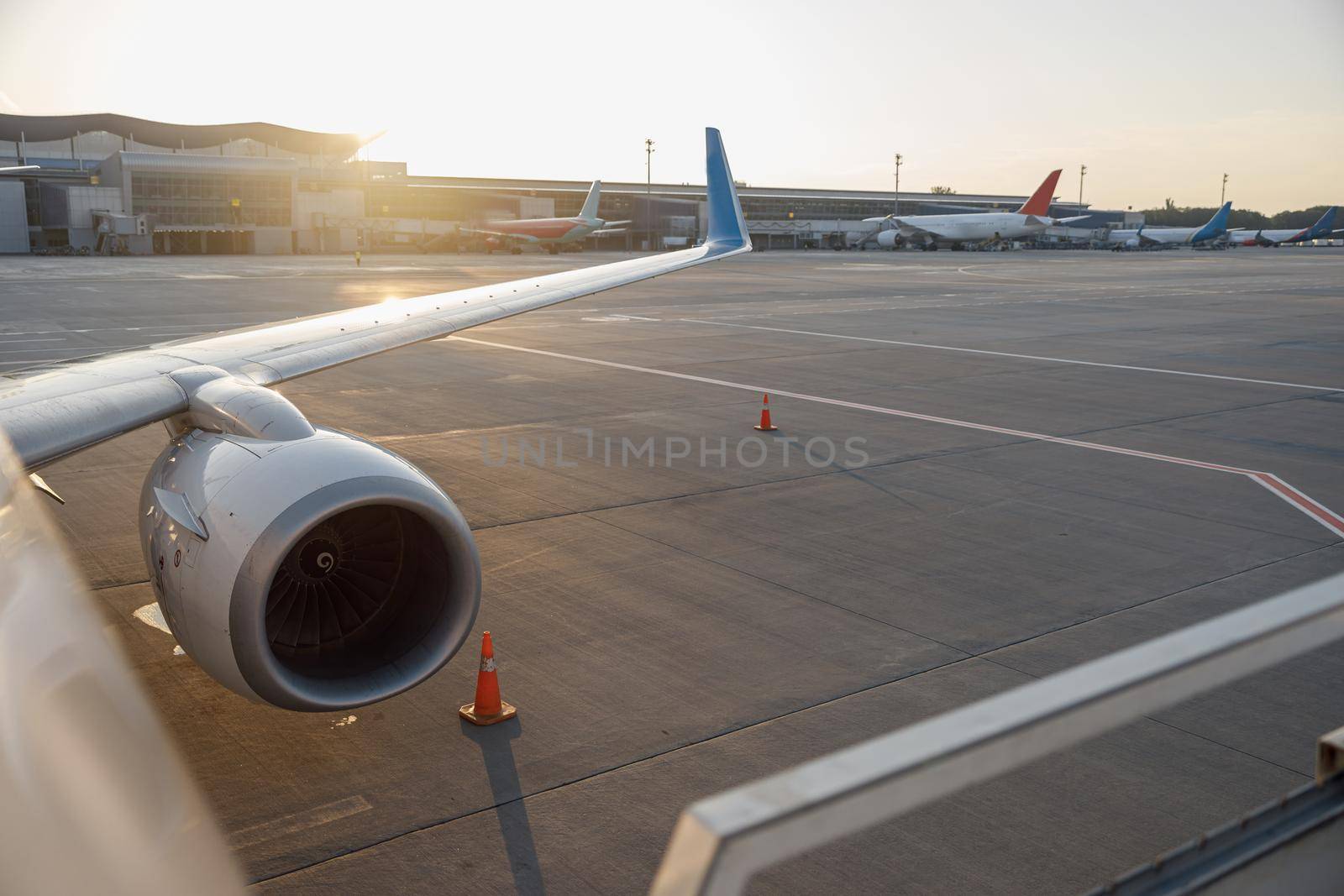 Close up shot of a wing of commercial airplane near the terminal in an airport at the sunset. Aircraft, traveling concept