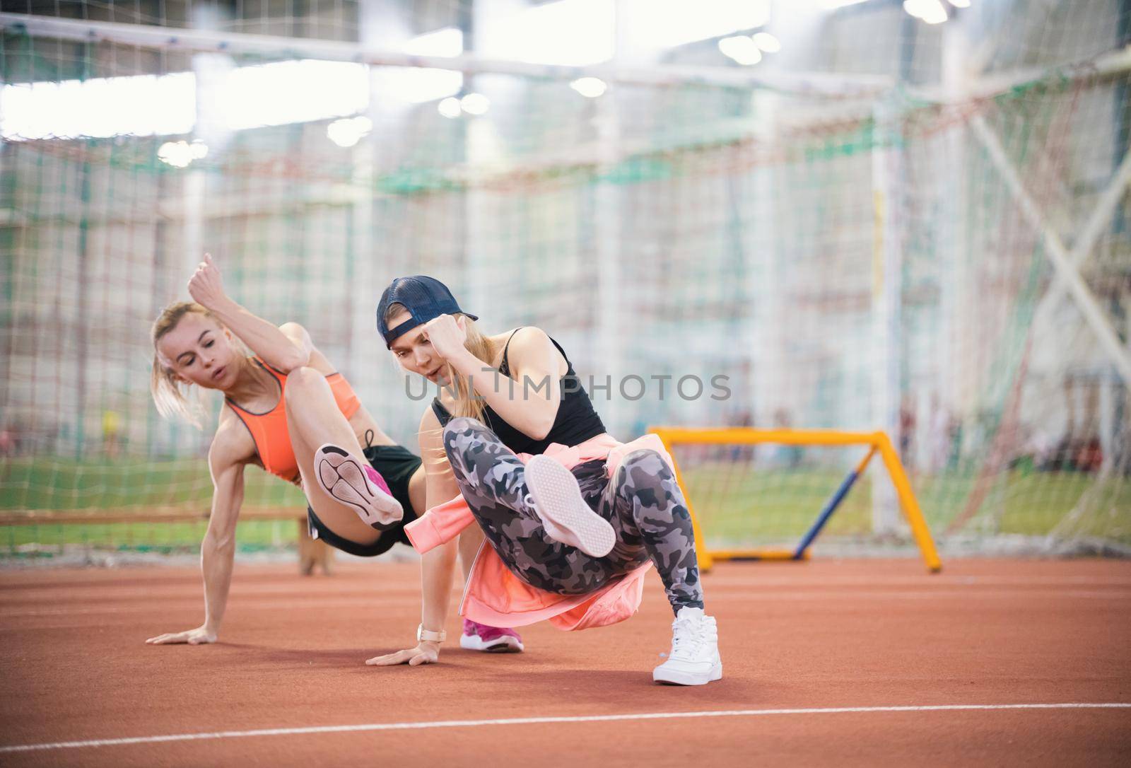 Two young beautiful women with blonde hair doing cardio exercises and breathing hard in the sports hall together, side view