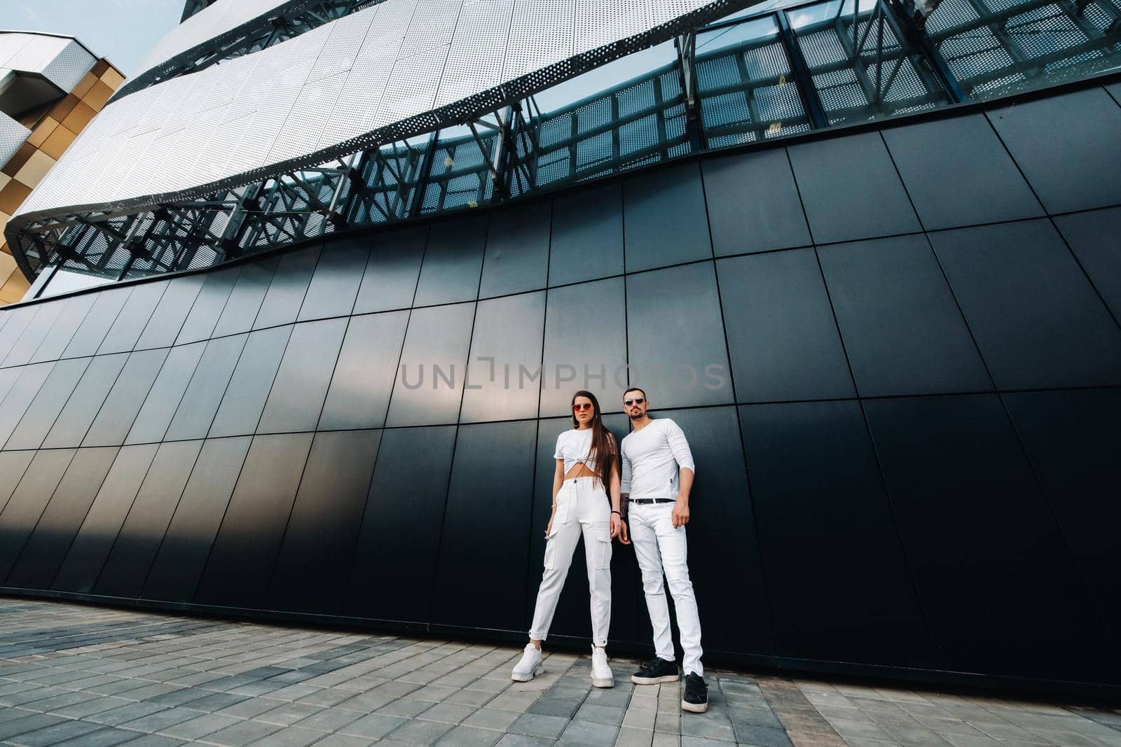 A girl and a guy walk around the city in white clothes and glasses, a couple in love against a black wall