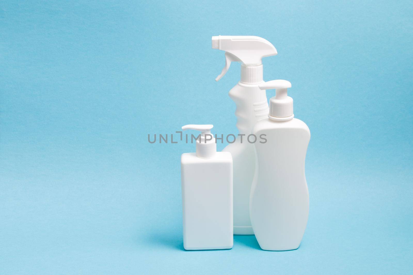 several white plastic bottles with different types of dispensers on a blue background, two white unbranded dispenser bottles and a spray bottle