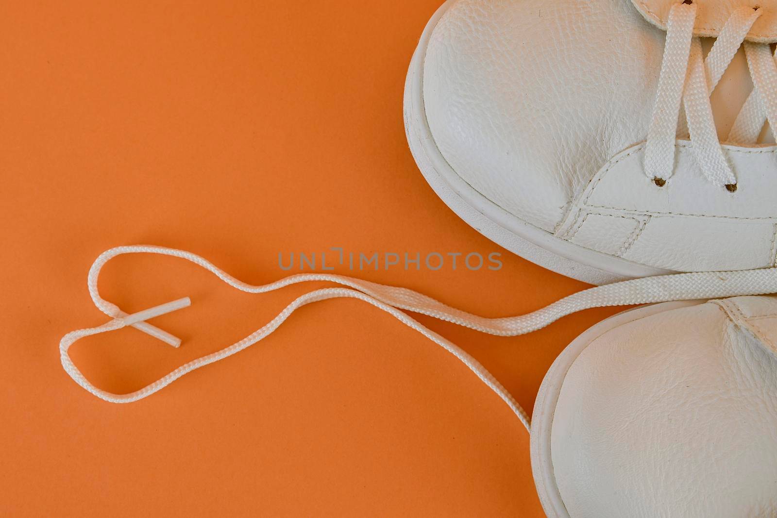 Pair of white shoes with heart made of shoelaces on orange background. Trendy summer color. Trendy summer bold color image . Copy space