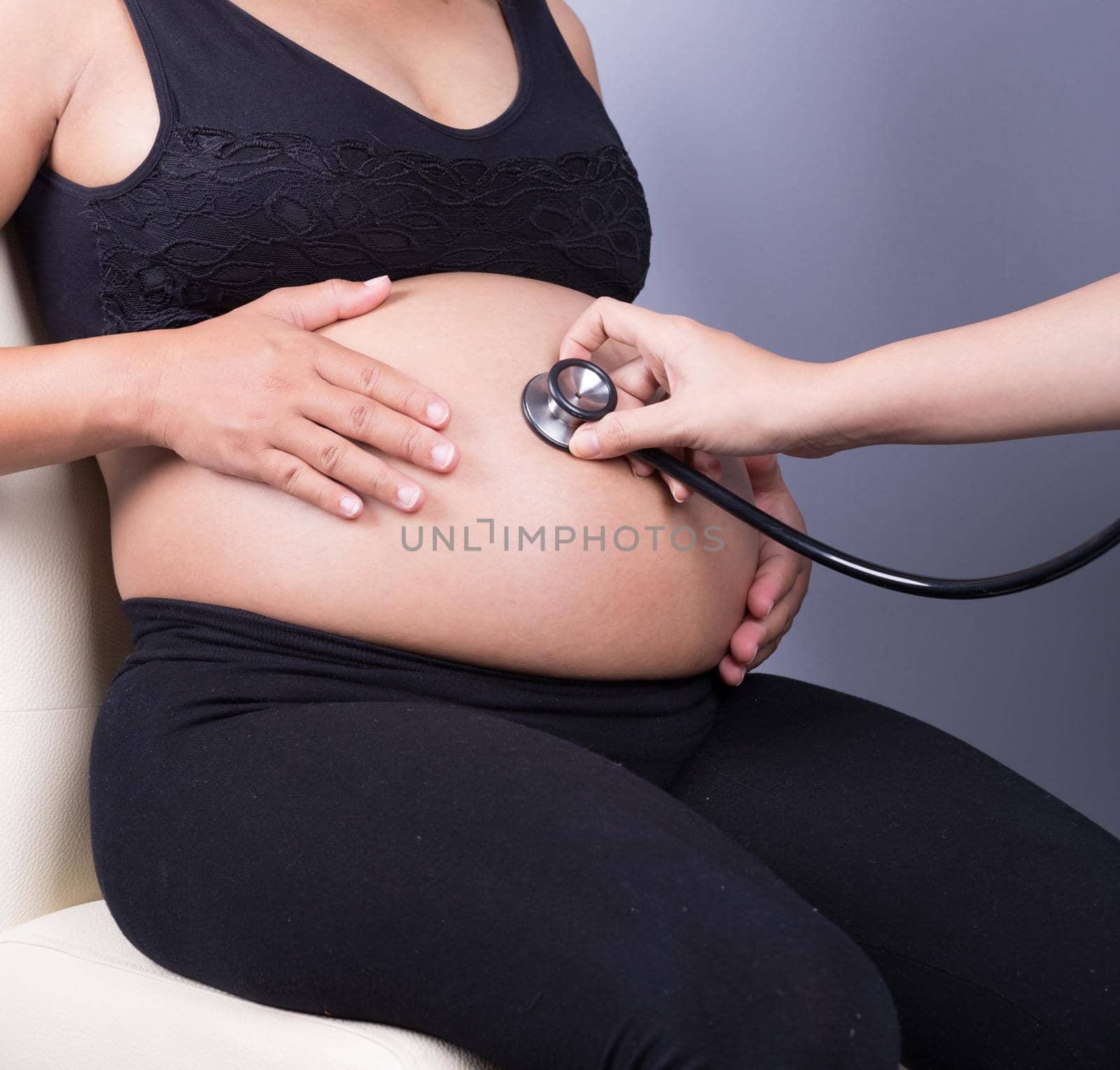 Belly closeup of a pregnant woman examined with a stethoscope