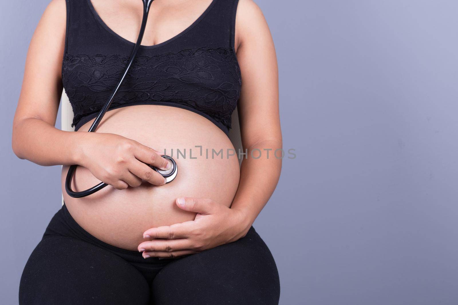 close-up of a pregnant woman with stethoscope listening belly to baby