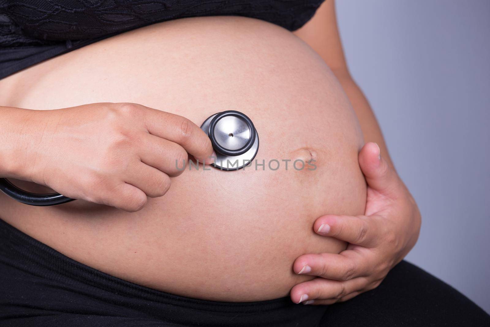 close-up of pregnant woman with stethoscope listening belly to baby