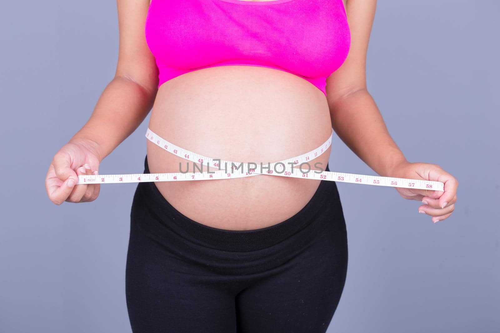 close-up belly of Pregnant woman with measuring tape on gray wall background