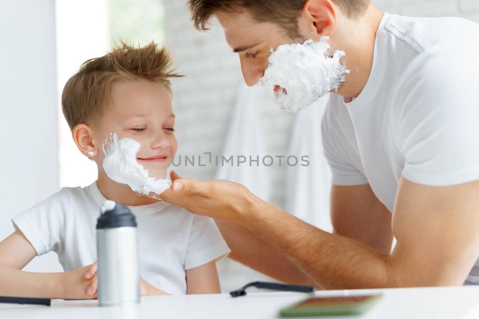 Father teaches his little son how to shave face in bathroom