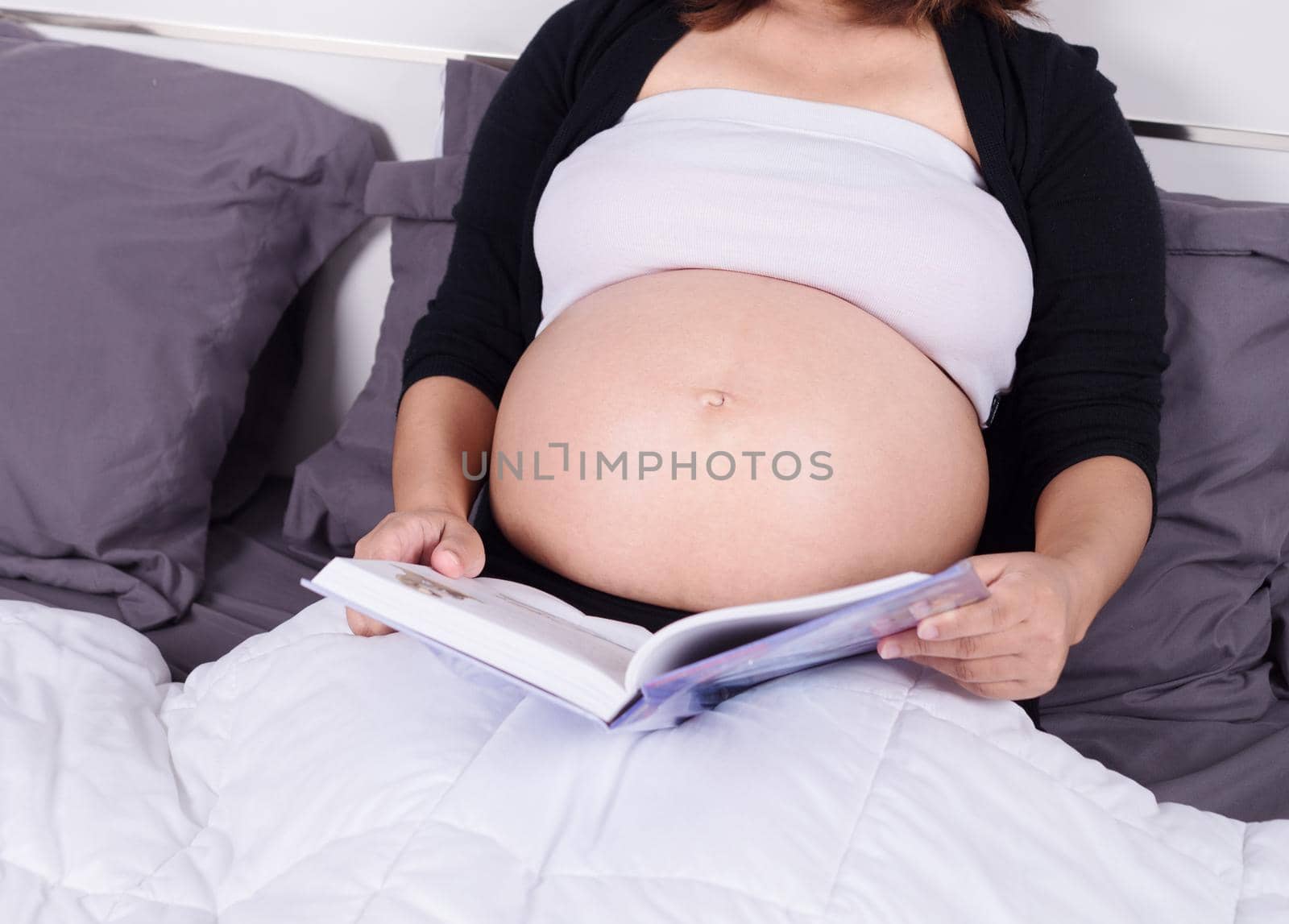 close up pregnant woman reading a book while lying on a bed in the bedroom at home