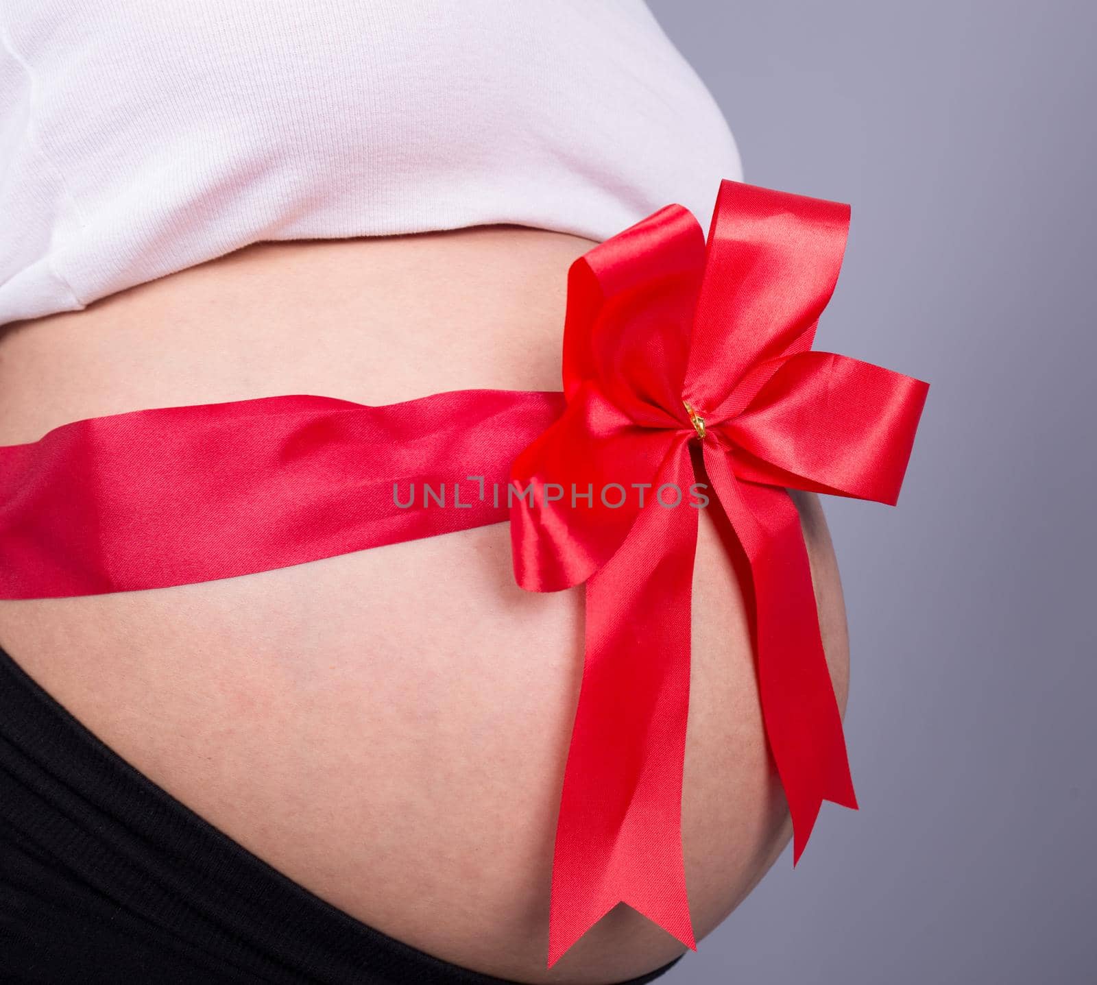 close up pregnant woman with red ribbon gift on belly by geargodz