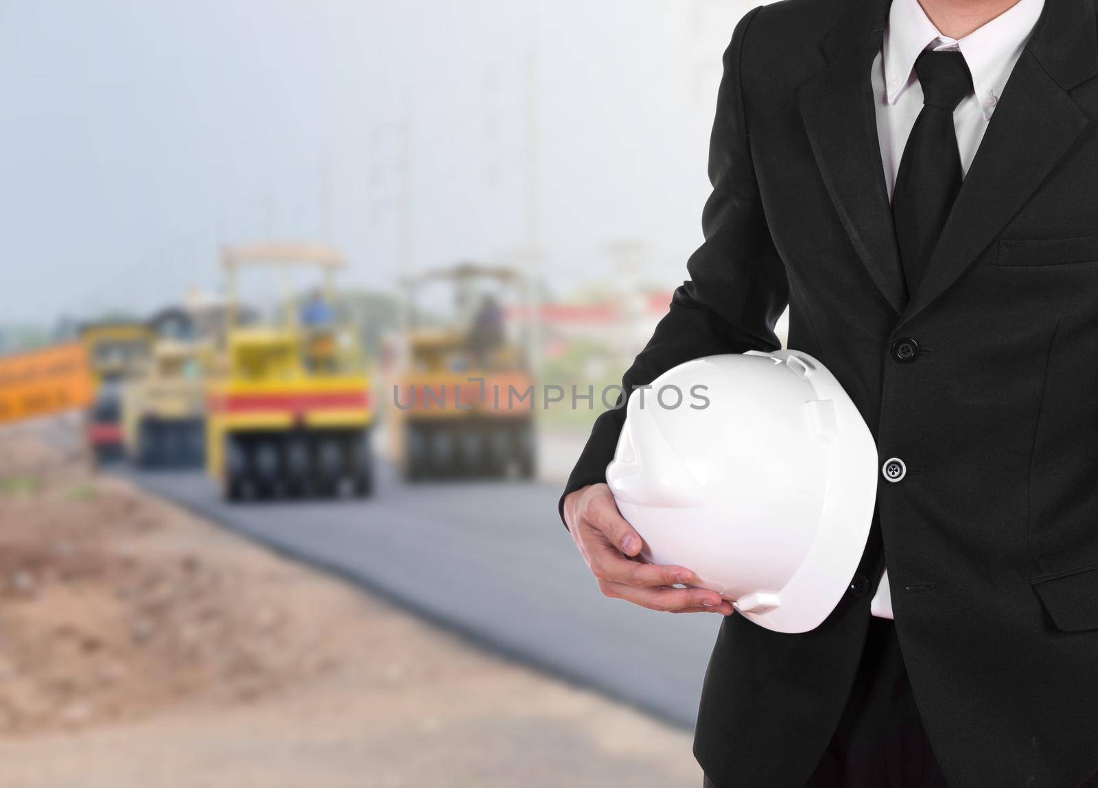 engineer in suit holding helmet with asphalt road under construction by geargodz