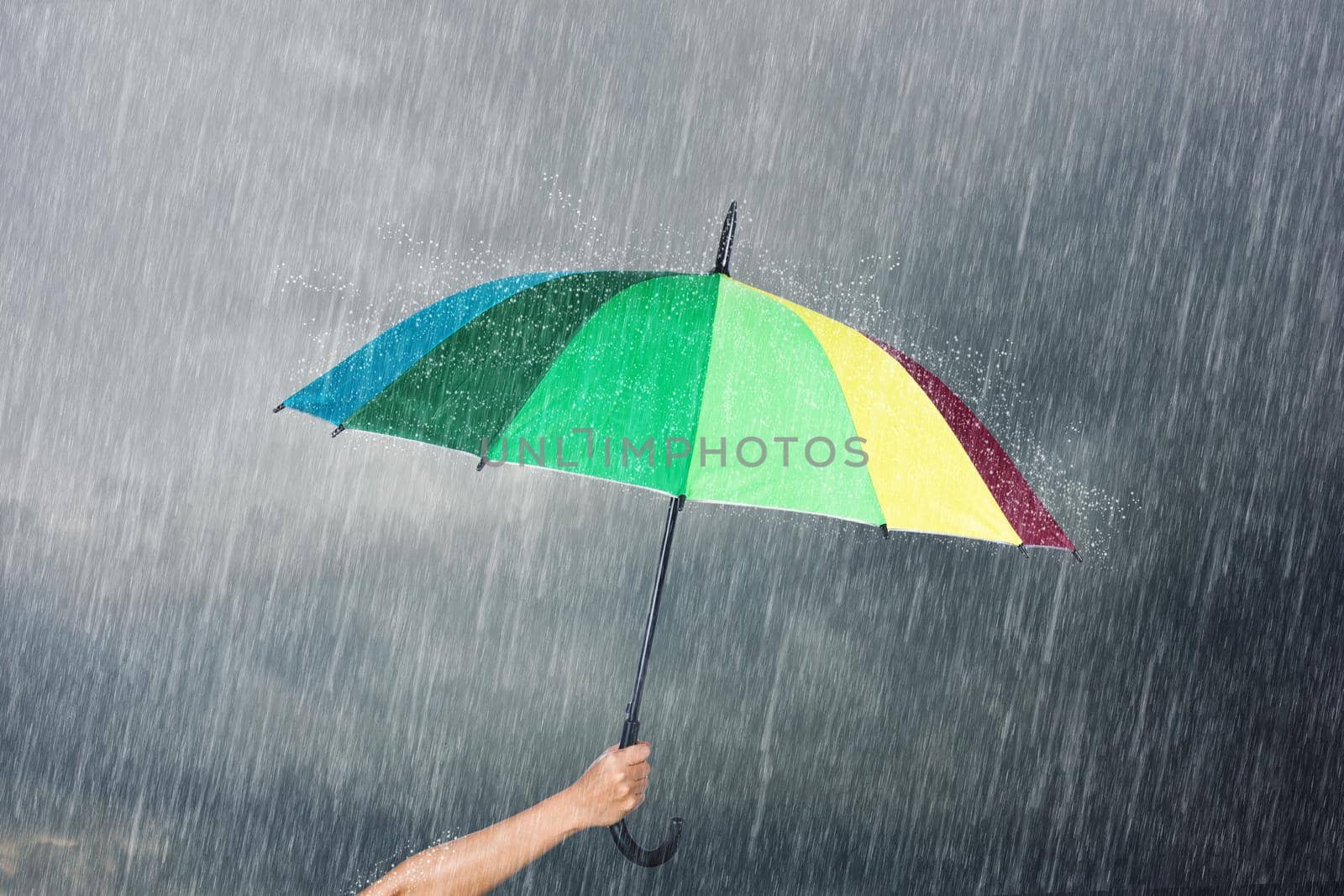 hand holding multicolored umbrella under dark sky with falling rain