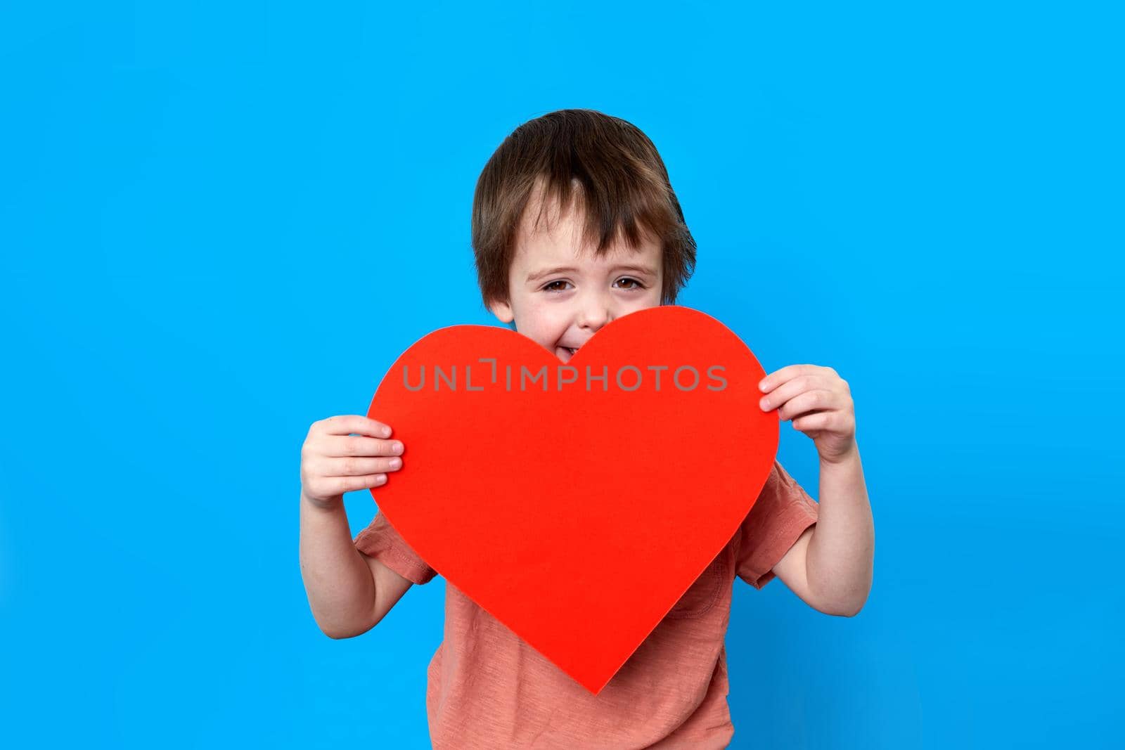 Portrait of stylish little boy holding big red heart blue background