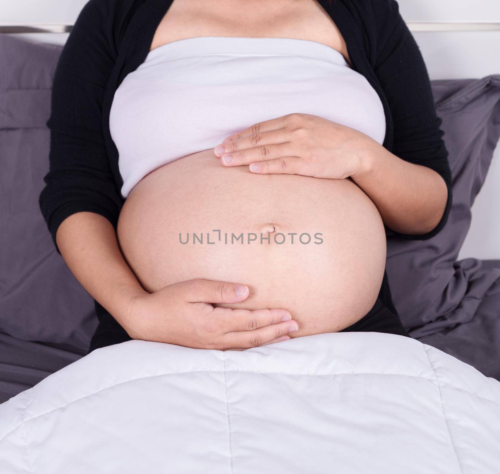 close up belly of pregnant woman sitting on bed in the bedroom at home