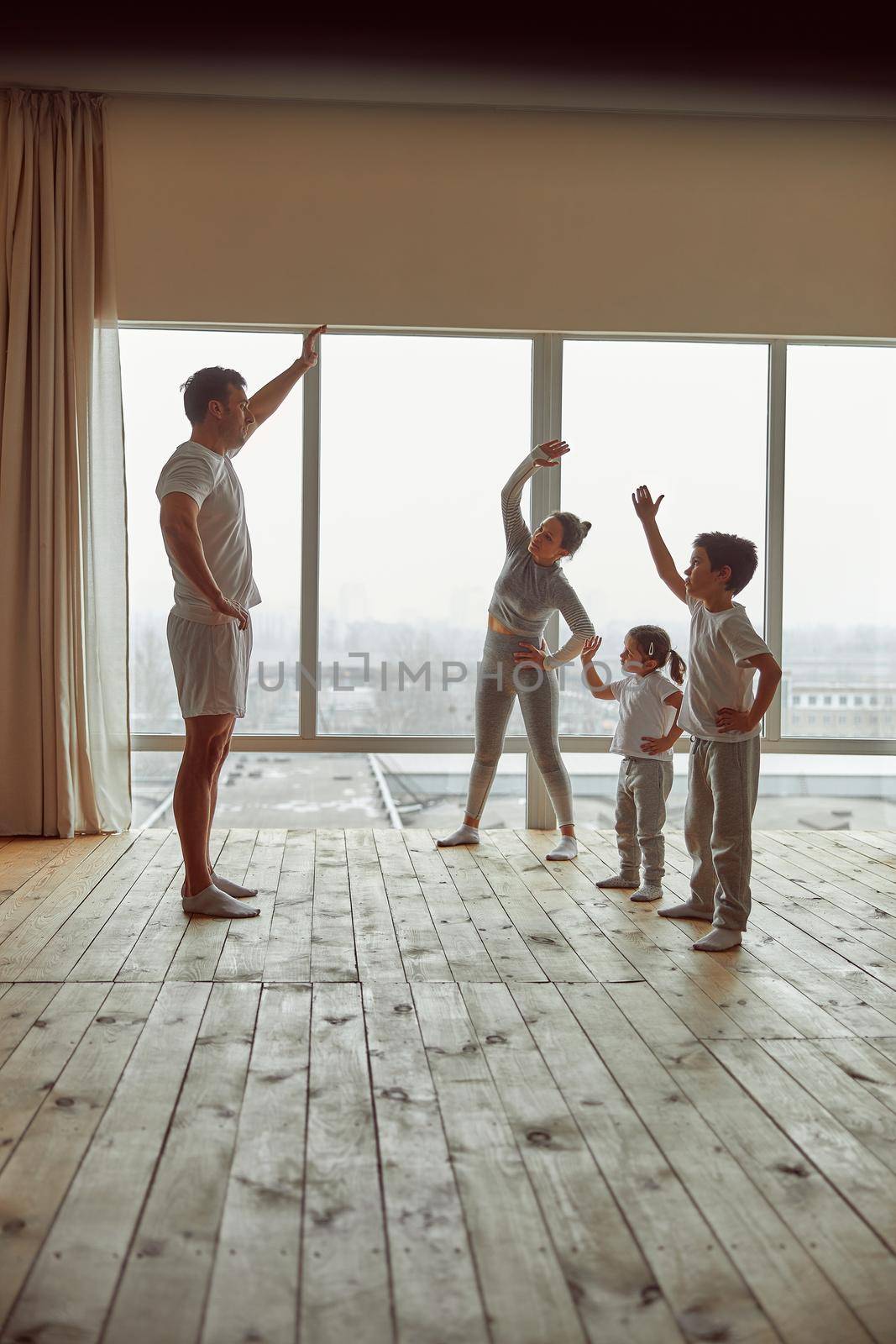 Father is teaching mom with son and daughter how to exercise during quarantine in living room