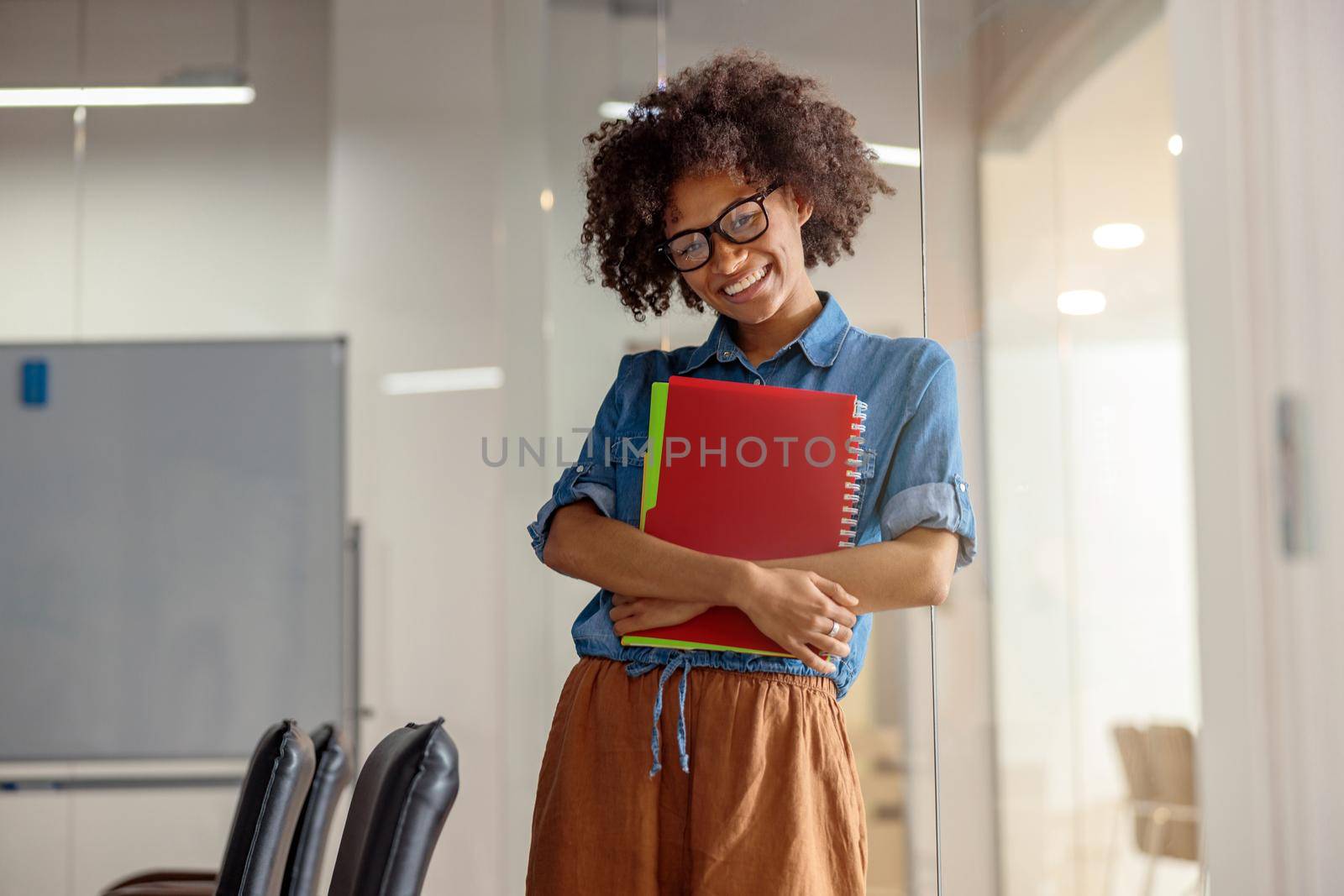 Smiling American lady standing in the office while holding documents and looking at camera