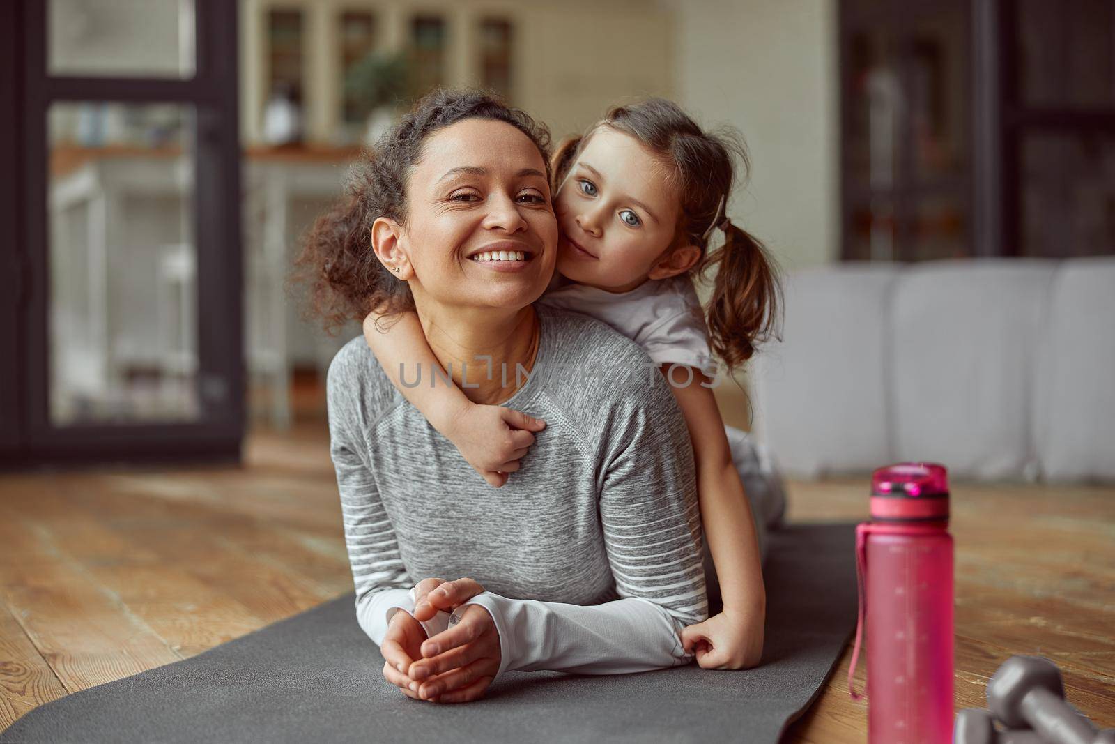 Waist up portrait of smiling girl hugging her mom while they are doing training at home