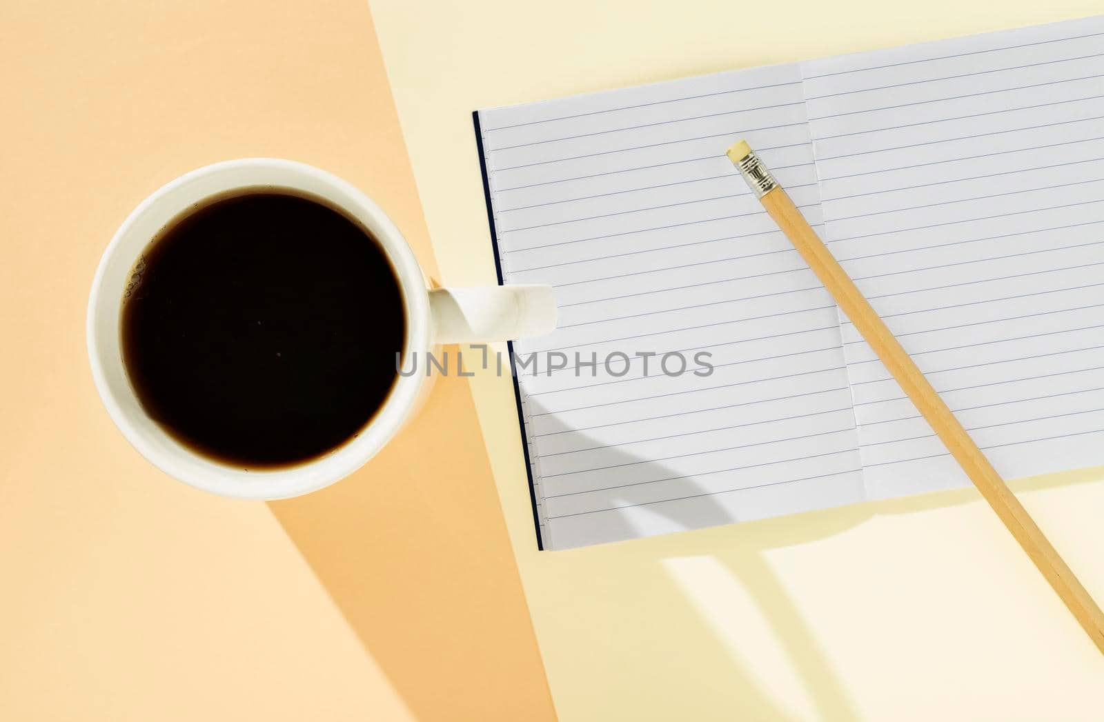 White mug with coffee  on colored background , opened  notebook with pencil on background