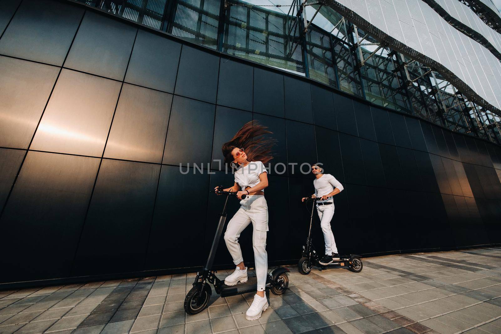 A girl and a guy are walking on electric scooters around the city, a couple in love on scooters