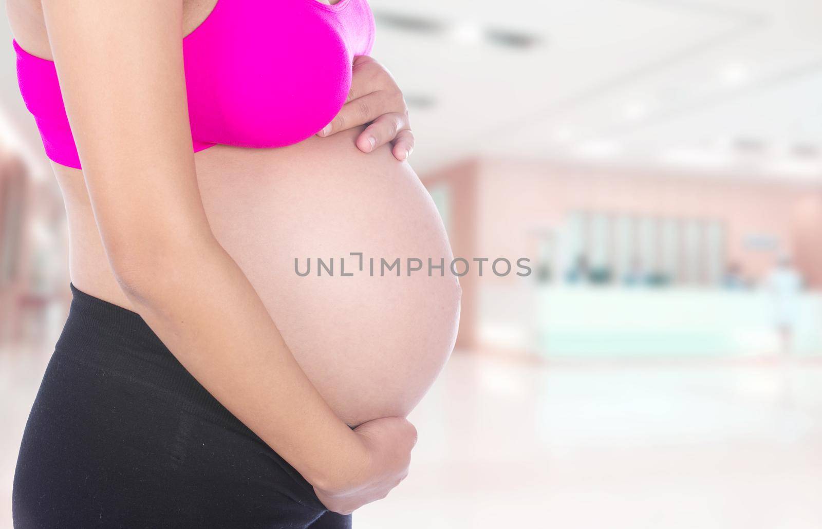 Close-up of pregnant woman belly with her hand on it in hospital background