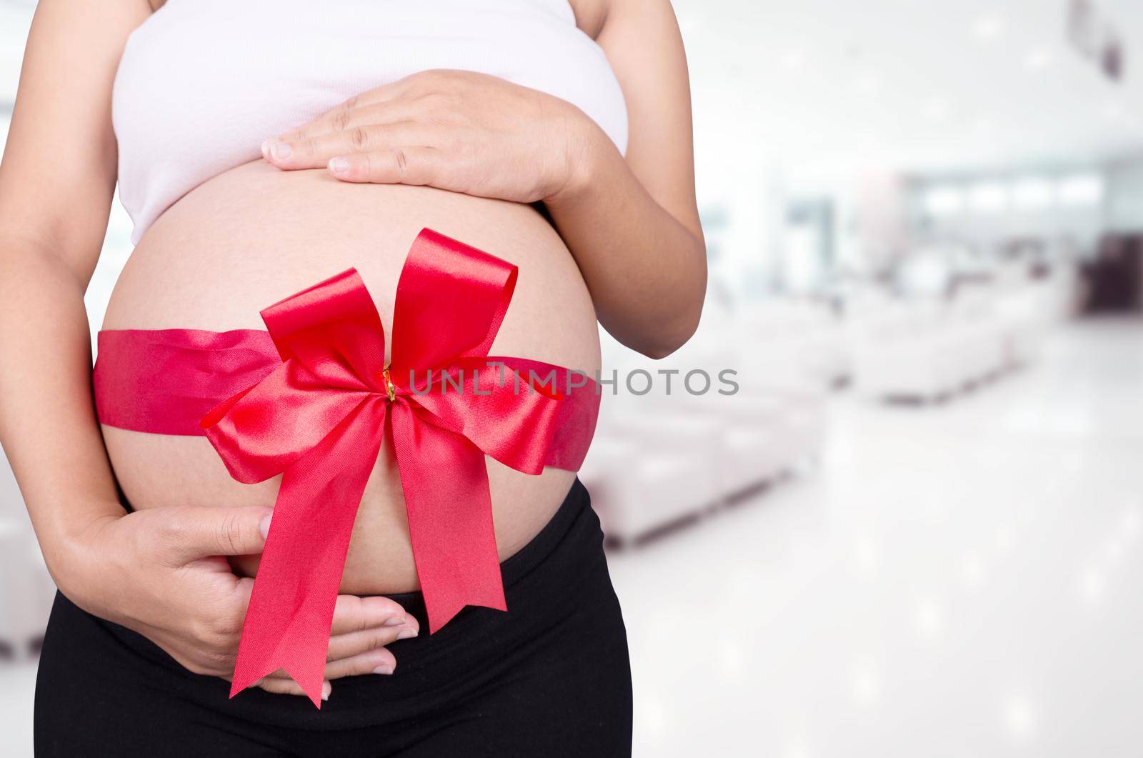 close up pregnant woman with red ribbon gift on belly in hospital background by geargodz