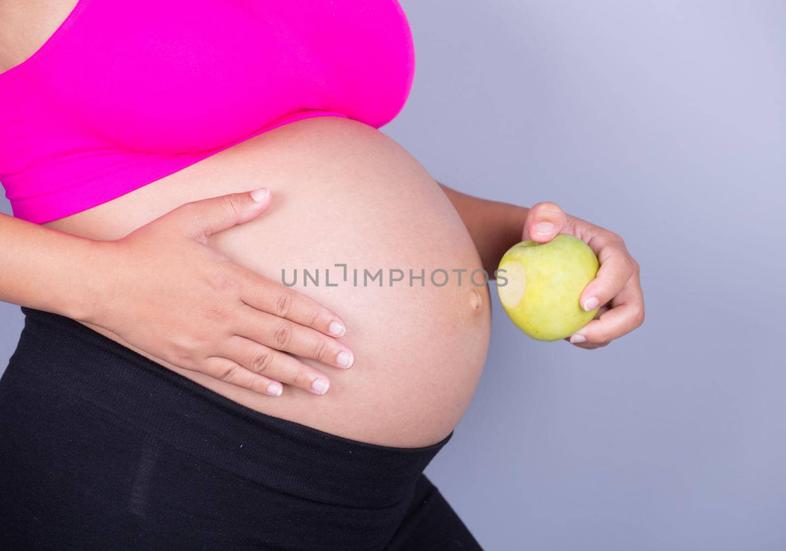 close-up belly of pregnant woman with green apple on gray background by geargodz