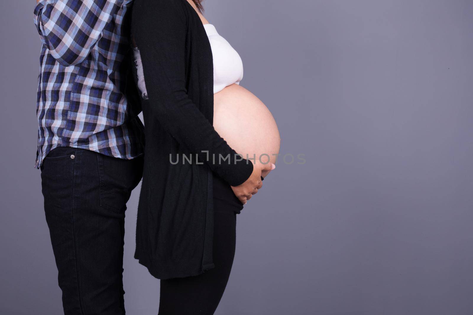 Pregnant woman with her husband on gray wall background