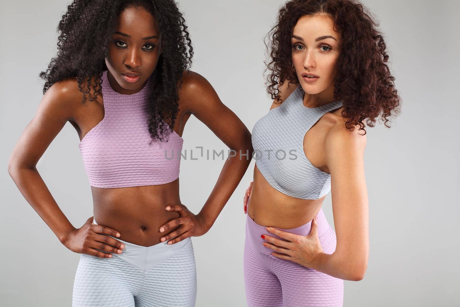 Attractive excited fitness girls in sportwear jumping of joy isolated over light background