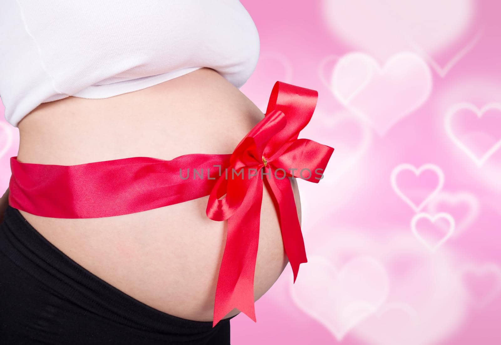 close up pregnant woman with red ribbon gift on belly on heart backrground