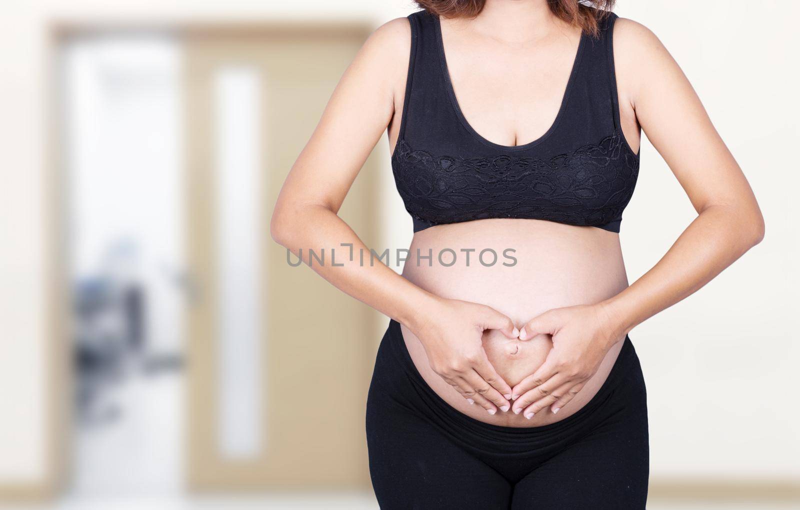 Pregnant Woman holding her hands in a heart shape on her belly in hospital background