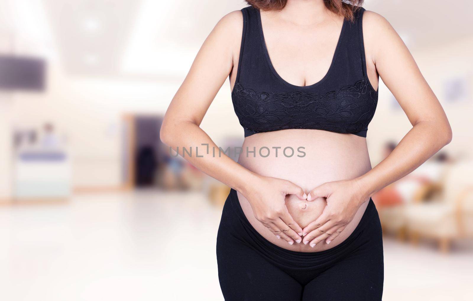 Pregnant Woman holding her hands in a heart shape on her belly in hospital by geargodz