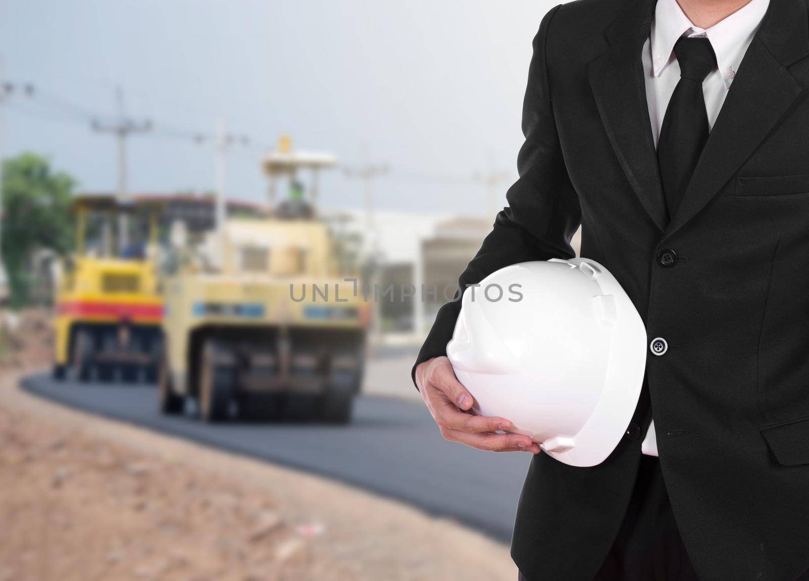 engineer in suit holding helmet with asphalt road under construction background