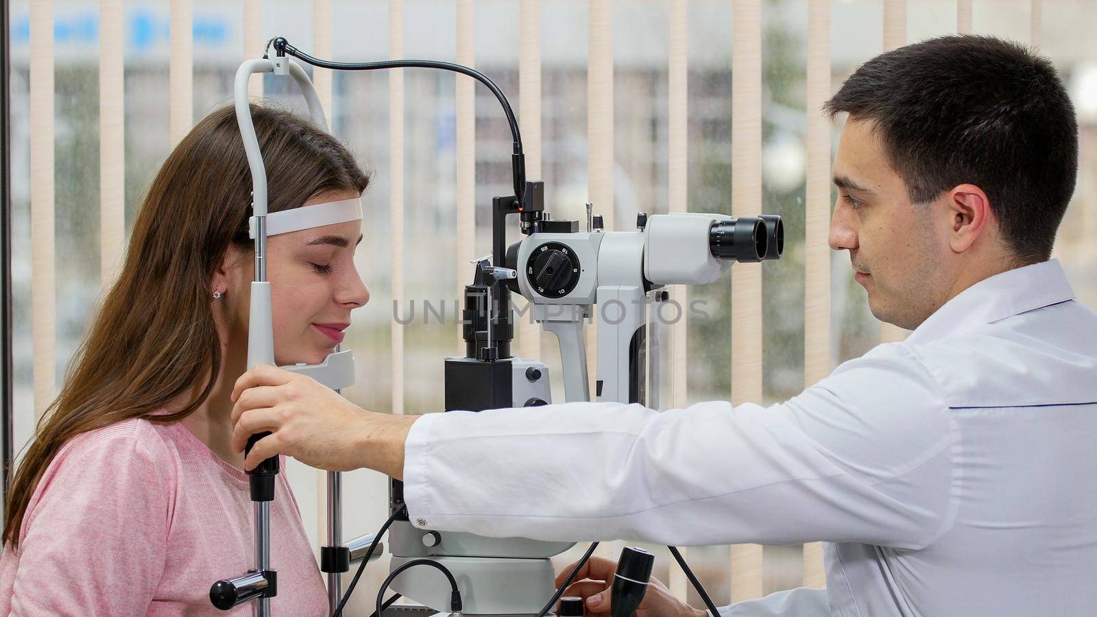Ophthalmology treatment - young smiling woman checking her visual acuity with a special equipment in the bright cabinet - put her chin on the stand. Mid shot