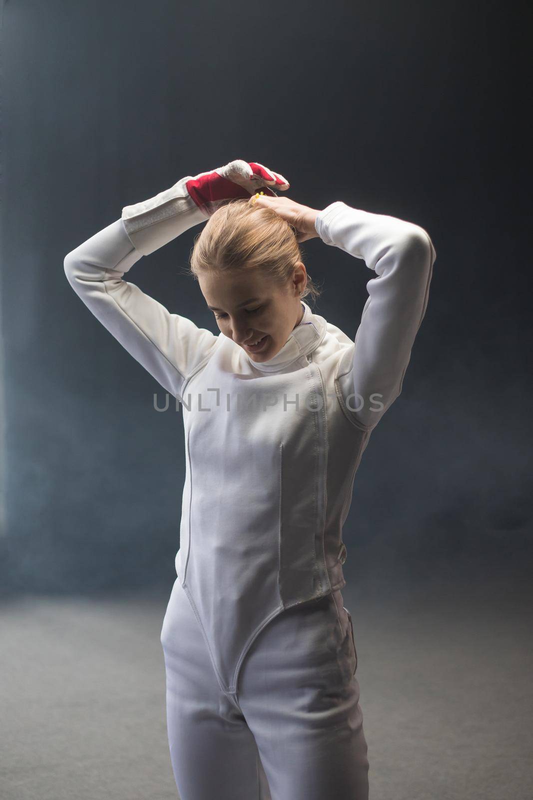A young woman fencer putting her hair up into a bun before the training. Mid shot