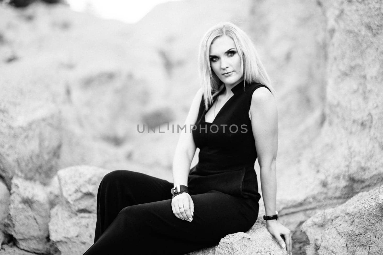 blonde girl in a black trouser suit with blue eyes on the background of a granite quarry from gray rubble