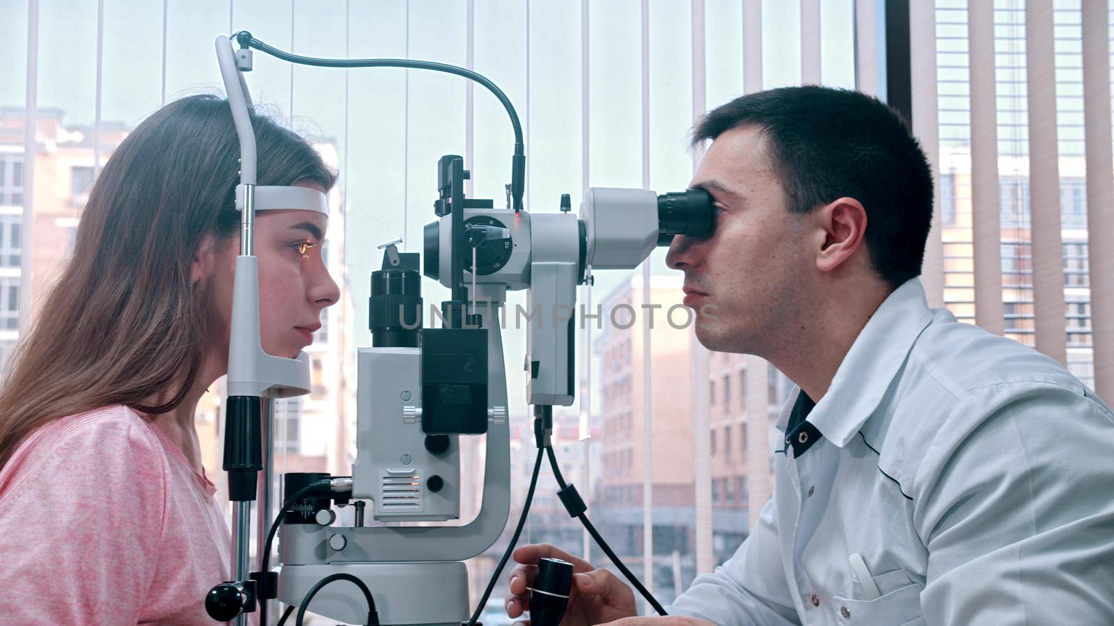 Ophthalmology - young pretty woman checking her visual acuity with a special equipment in the spacious cabinet. Mid shot
