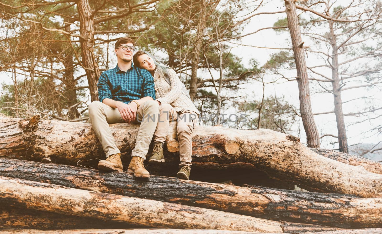 Casual style loving couple resting on stack of felled tree trunks in the forest