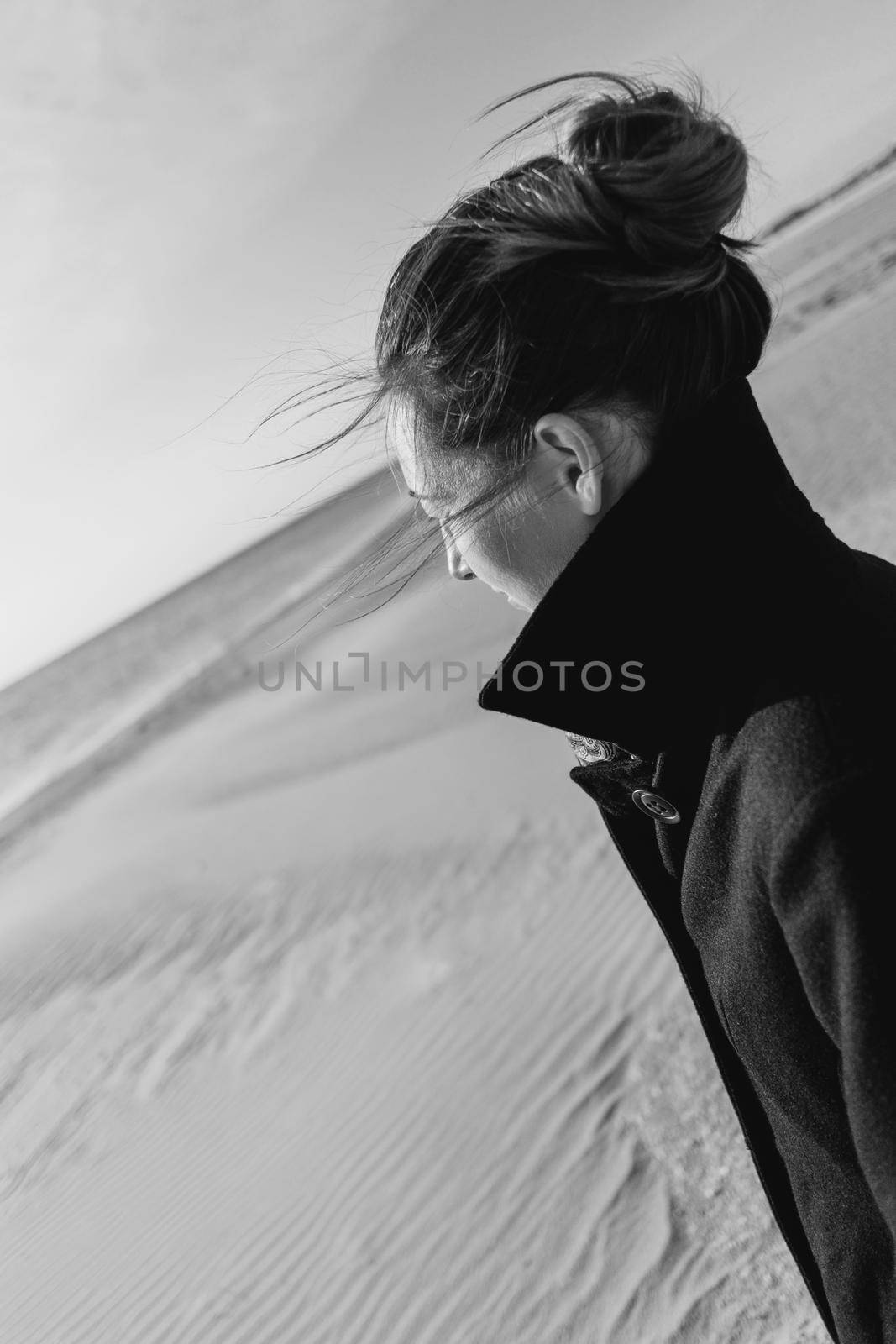 Young woman wearing in coat walking on sand beach and looking at sea. Monochrome image