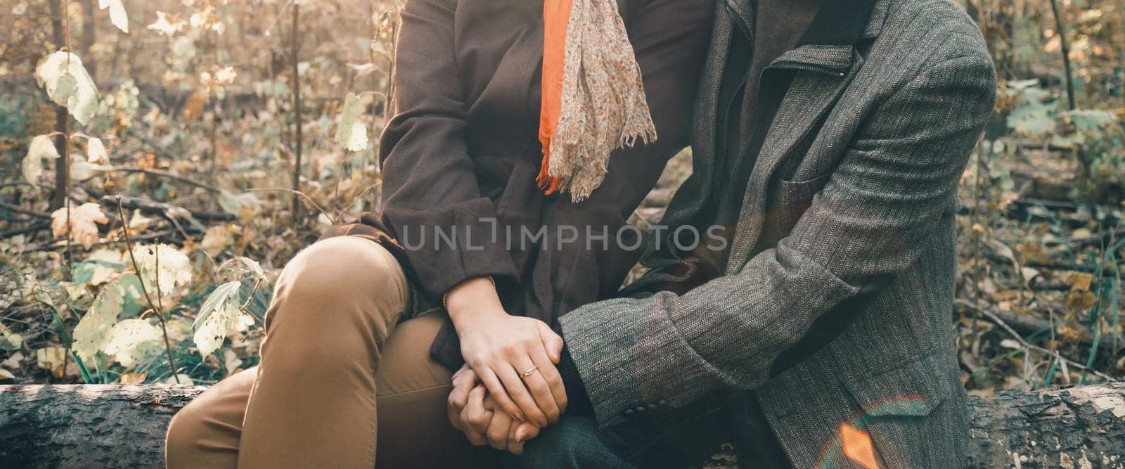 Unrecognizable loving couple resting in autumn forest and holding hands of each other