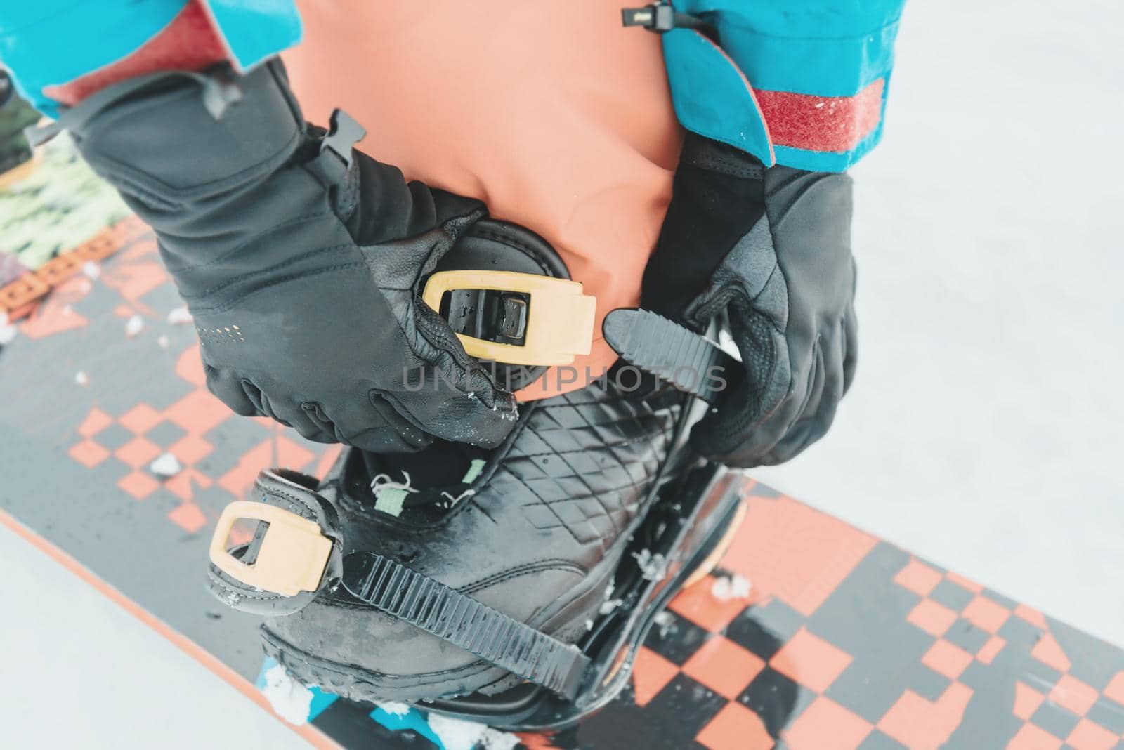 Woman putting on her snowboard and tightening the straps on background of snow in winter, close-up image