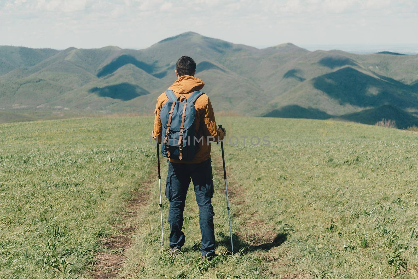 Explorer young man with backpack and trekking poles walking in the mountains