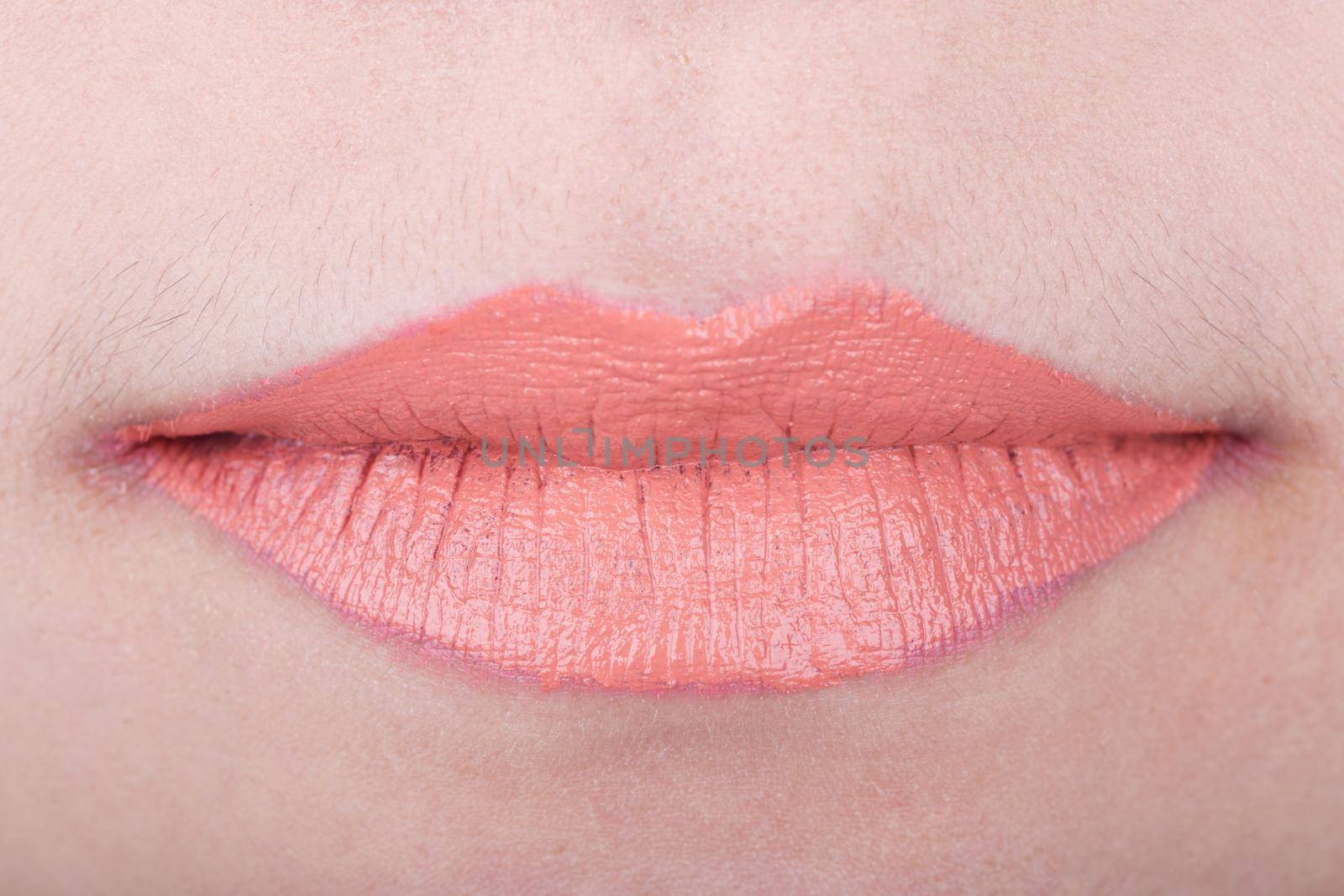 close-up of womans lips with orange glossy lipstick
