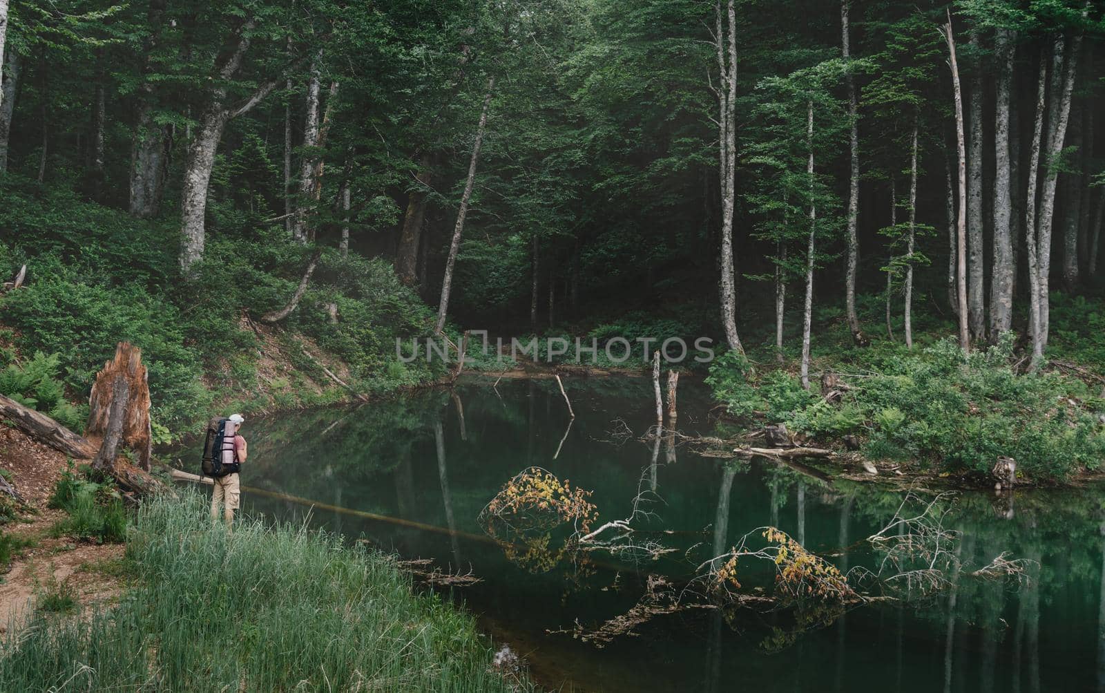 Hiker young man with backpack standing near a lake in the forest