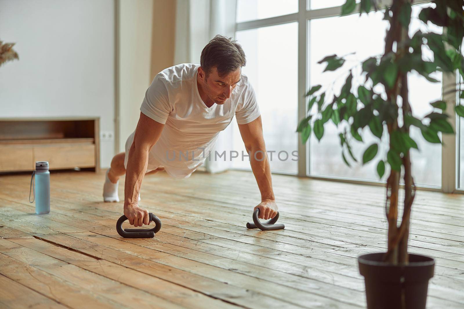 Sporty man doing push ups with equipment indoors by Yaroslav_astakhov