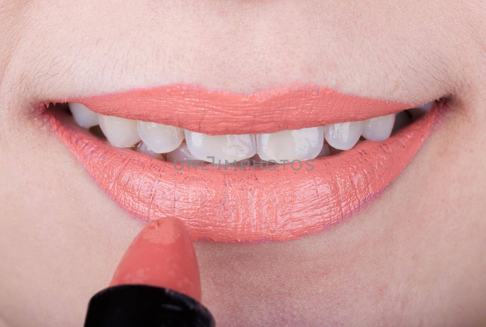 woman applying orange lipstick on her lips by geargodz
