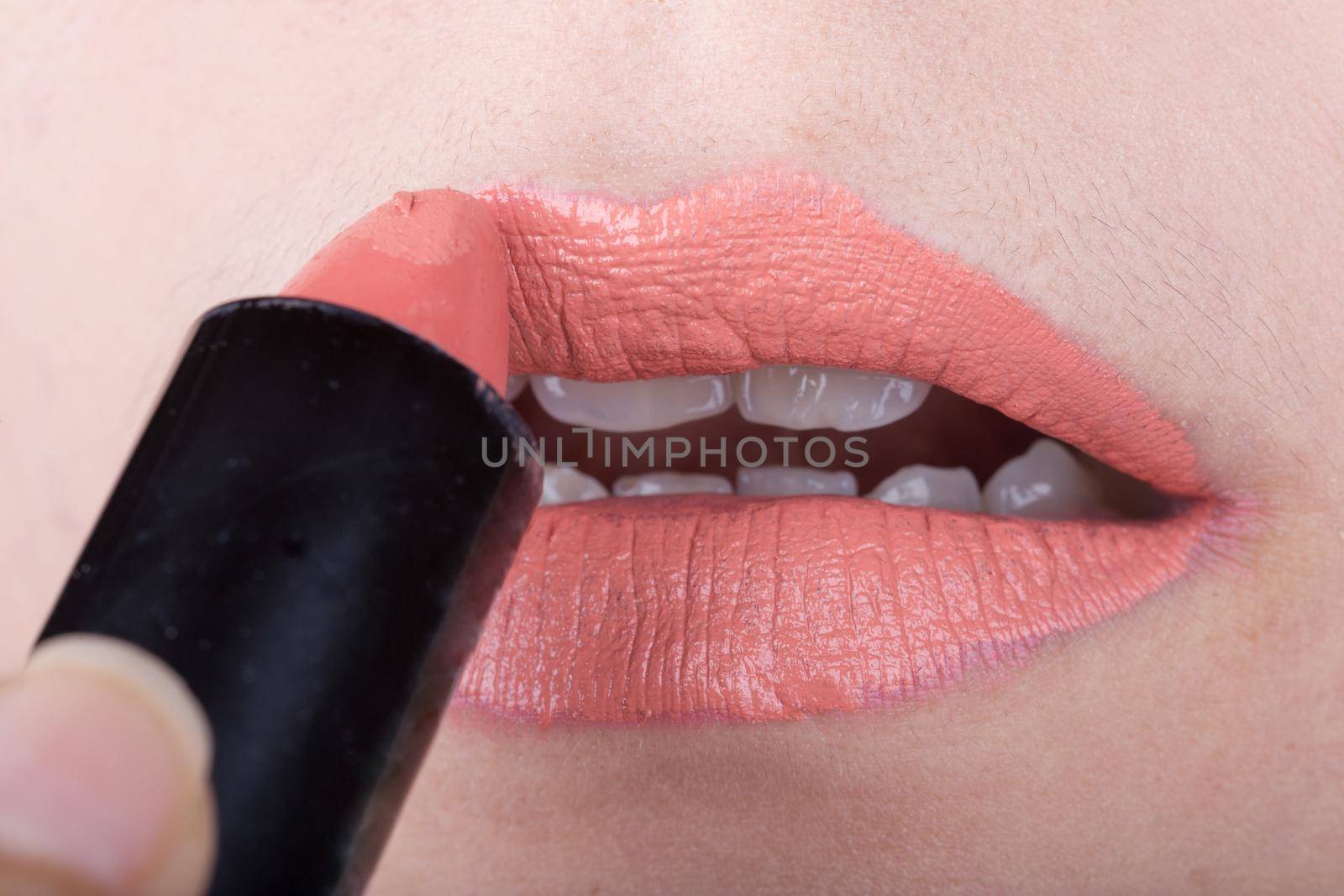 woman applying orange lipstick on her lips by geargodz
