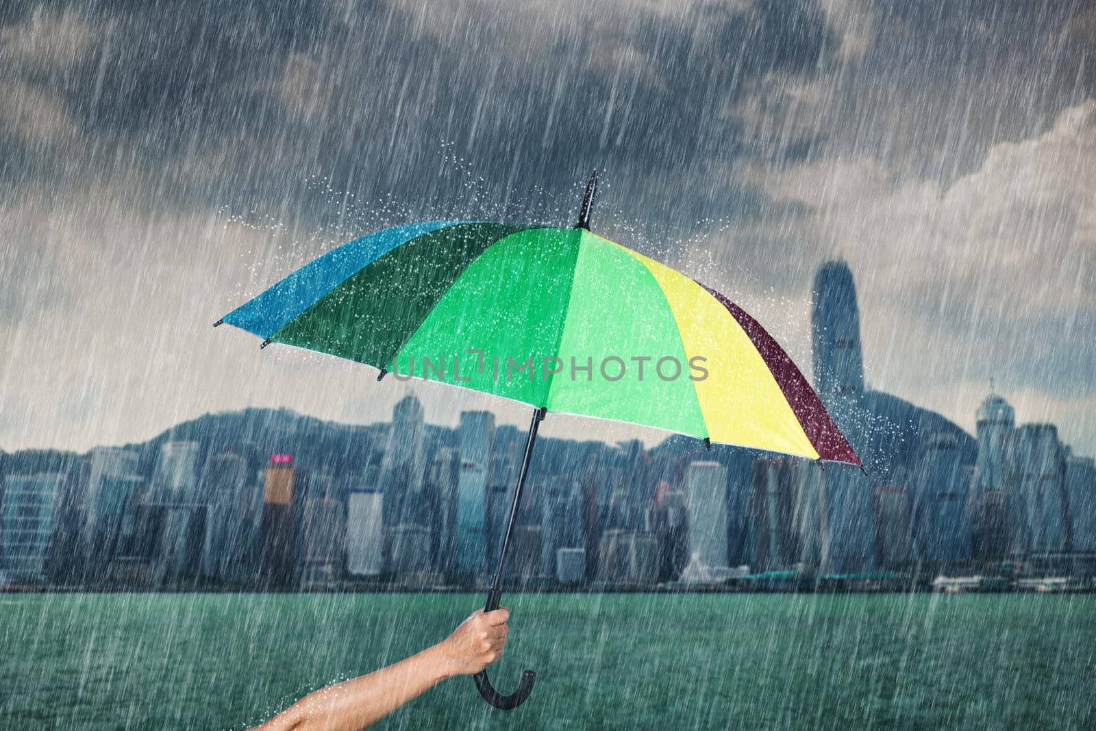 hand holding multicolored umbrella with falling rain at victoria harbour, Hong Kong